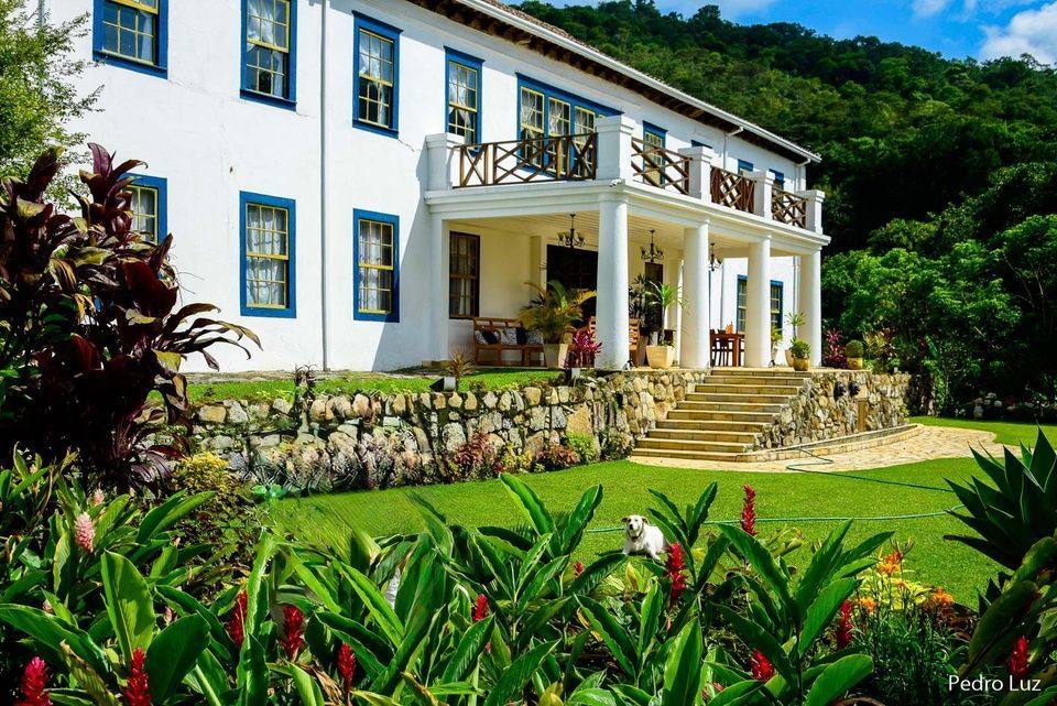 Fachada histórica do Casarão Penedo com jardim tropical e montanhas